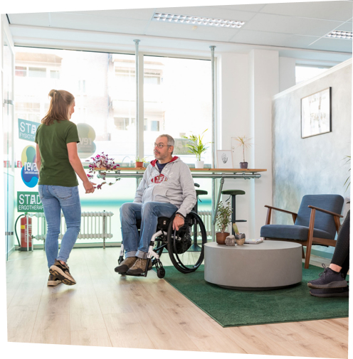 Fysiotherapeut haalt patiënt in rolstoel op uit wachtruimte bij STADS Fysiotherapie